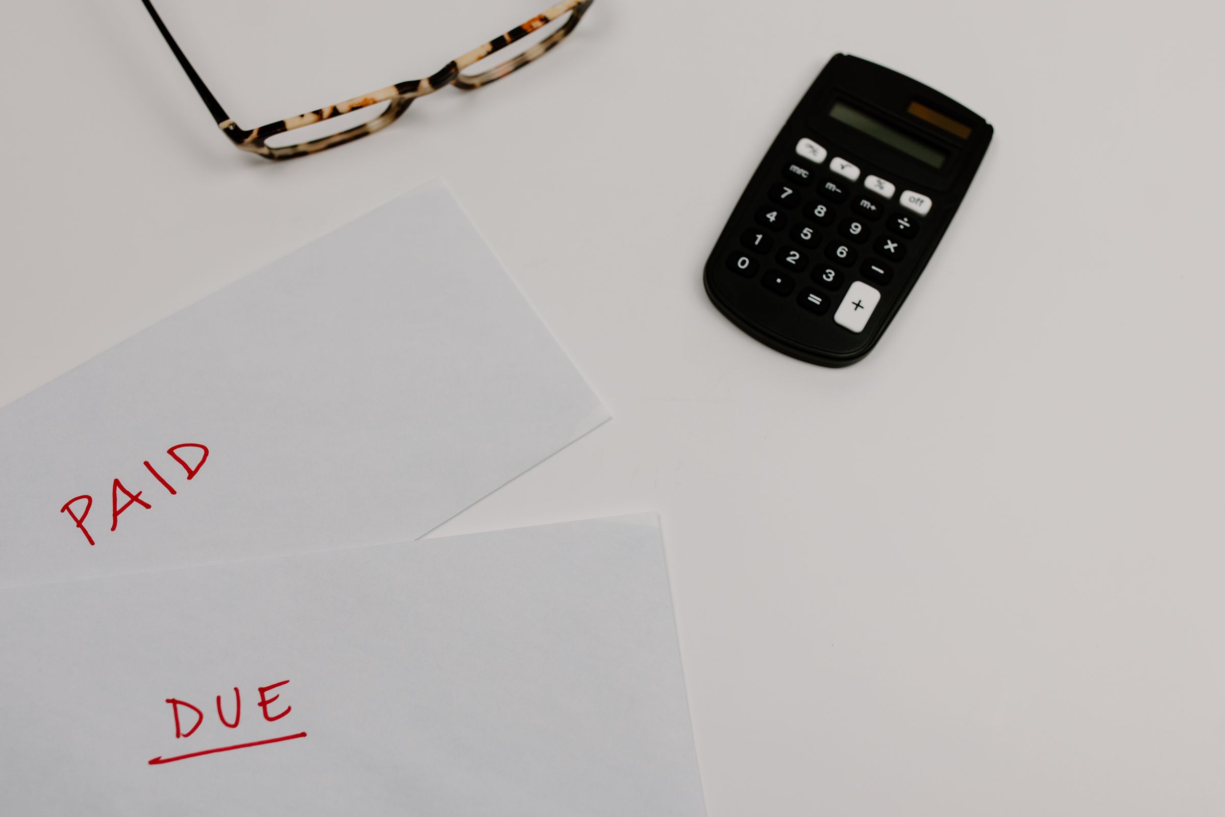 Documente financiare marcate Platit si De plata langa un calculator si ochelari.
